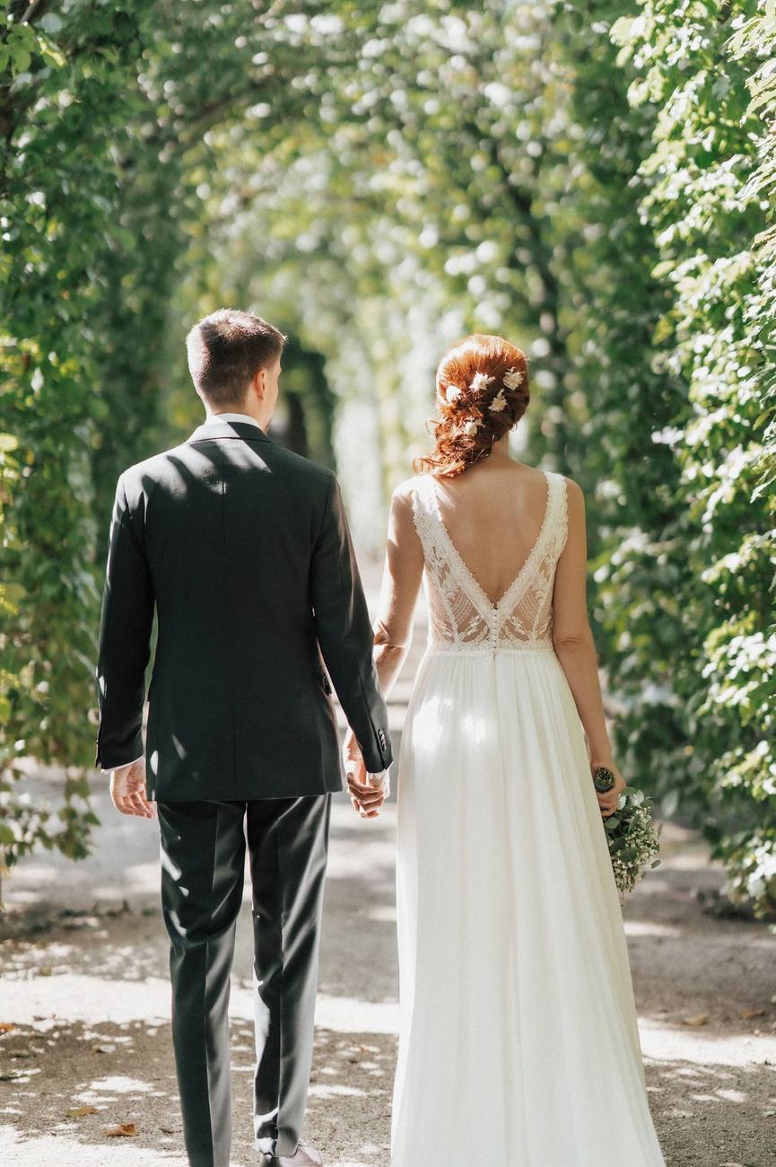 Novios caminando de espaldas bajo un túnel de árboles